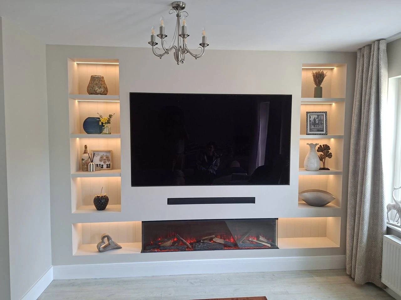 Custom built-in media wall with TV, soundbar, electric fireplace and lit shelving