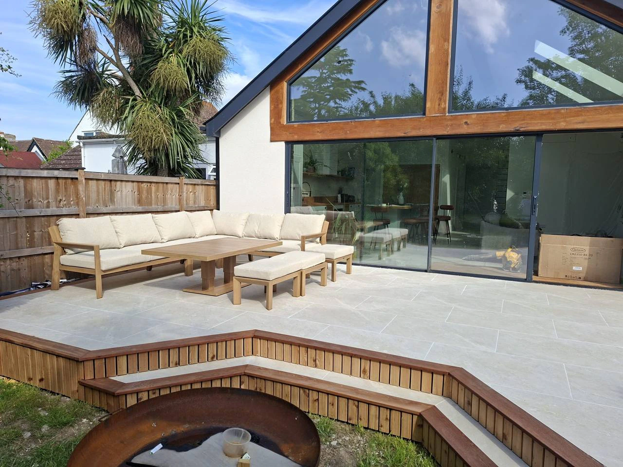 Modern patio with wooden outdoor sofa set, fire pit and glass rear extension