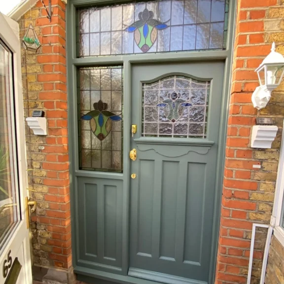 Restored 1920s front door in sage green with stained glass, in a red brick porch